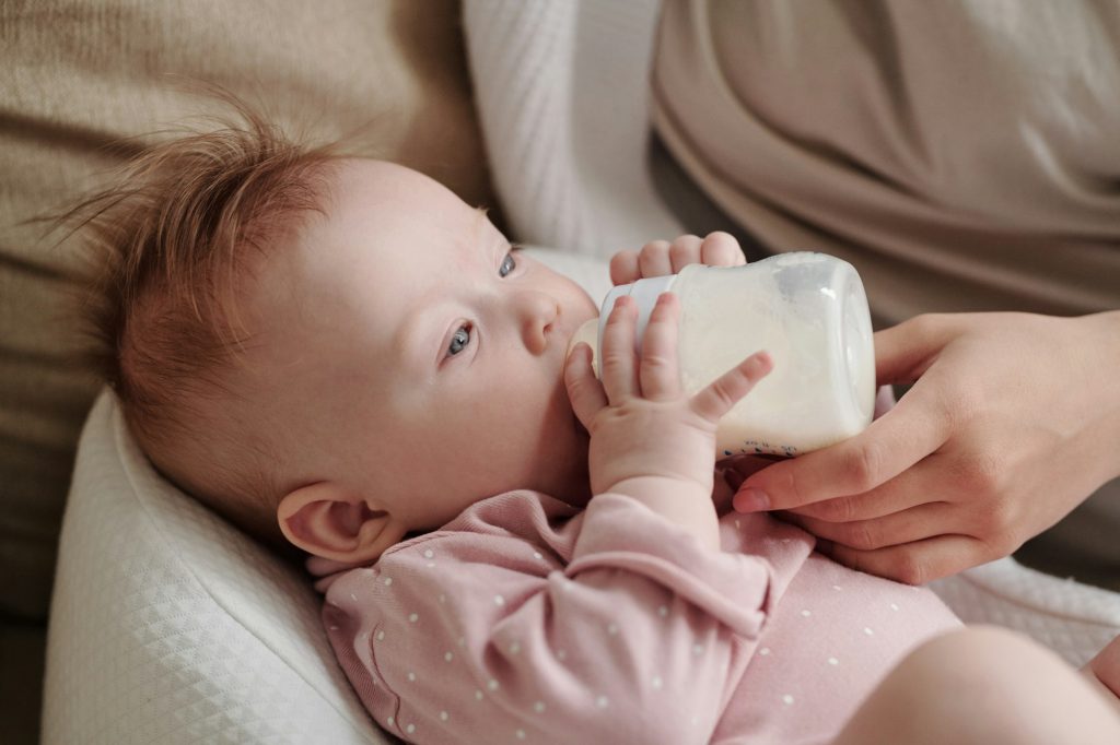Cute toddler girl eating milk while holding bottle