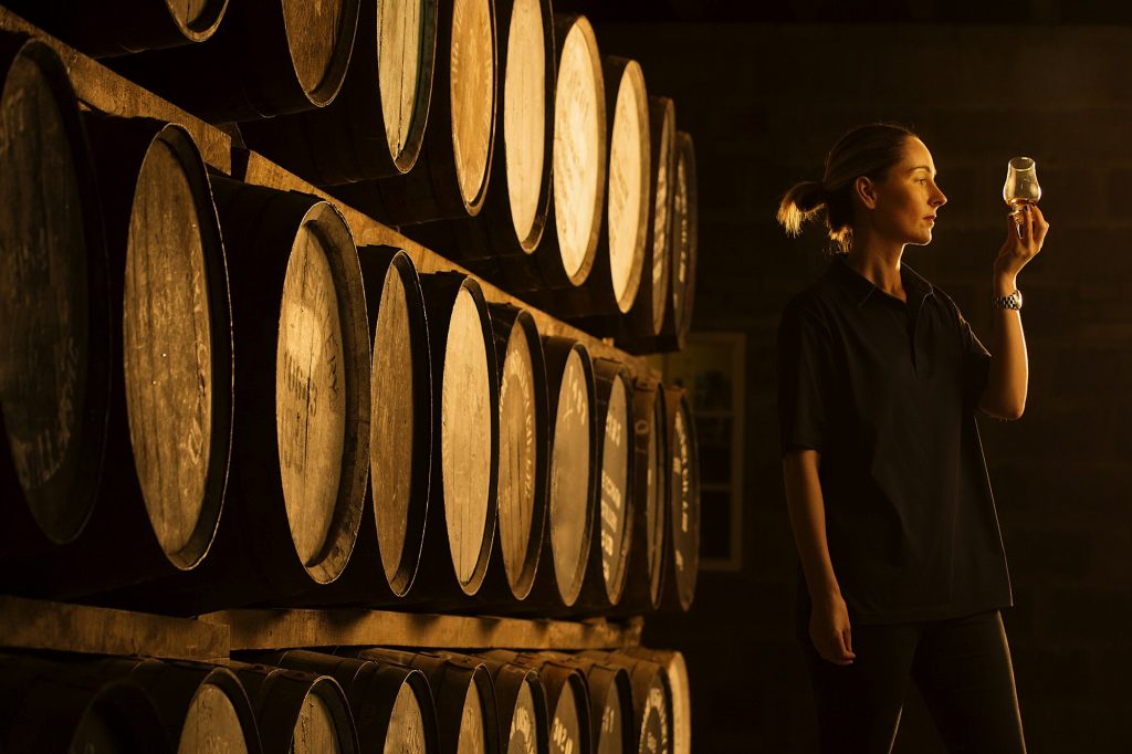 Female taster looking at the colour of whisky in glass at whisky distillery