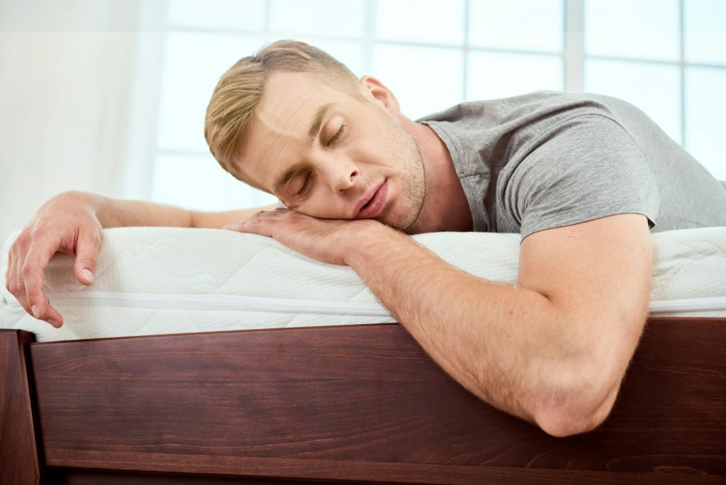 Having a nap. Young handsome man sleeping on a big and comfortable orthopedic white mattress in
