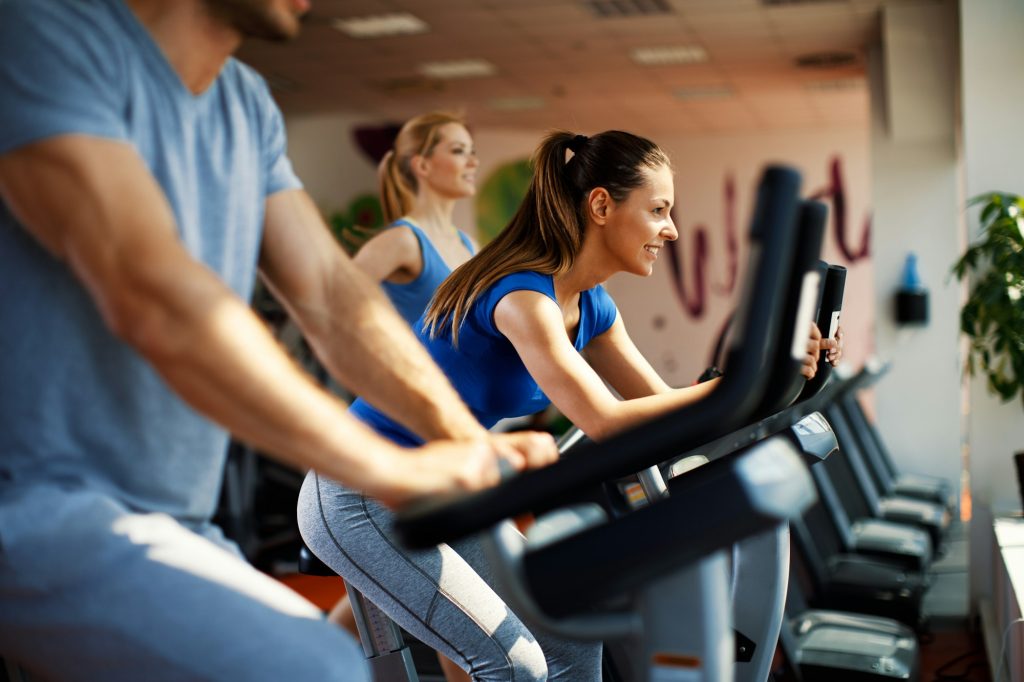 Young woman and man warming up on bikes in the gym
