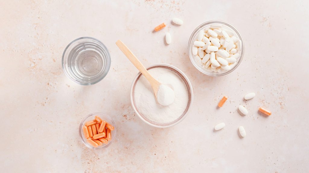 Collagen powder, pills and glass of water on beige stone table top